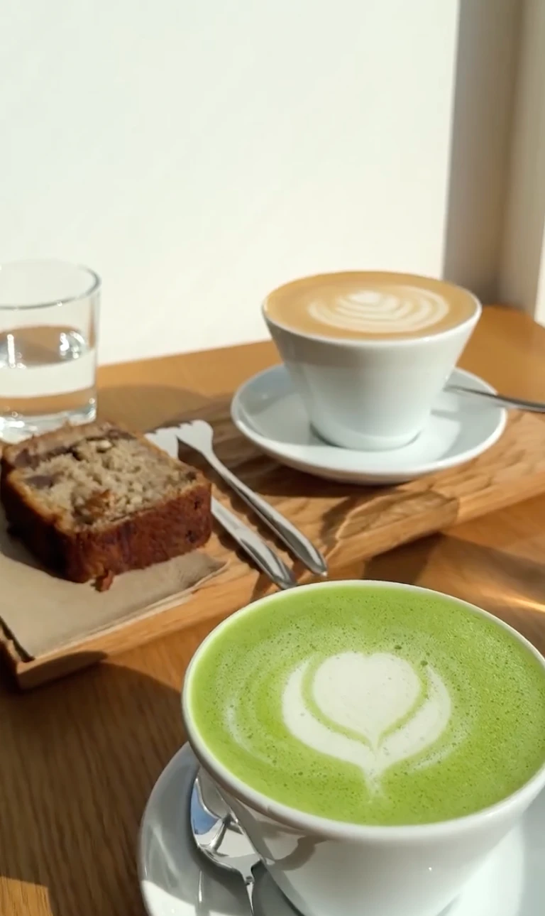 Matcha Latte, Cappuccino und Bananenbrot auf einem Holztisch.